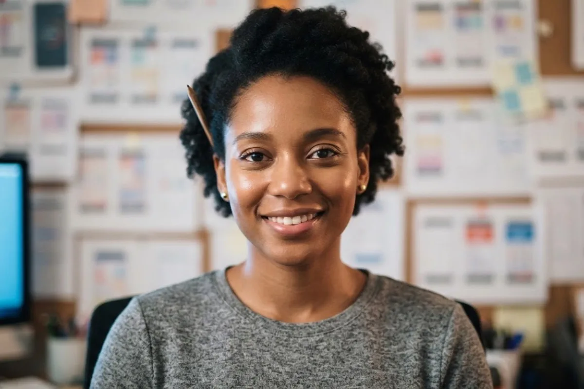 A product designer smiling at the camera in front of a wall of pinned layouts.